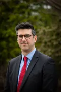 Headshot of a person wearing and suit and tie with trees in the background